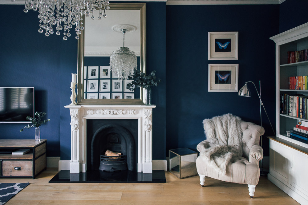 Dark blue sitting room with statement fireplace and glass chandelier