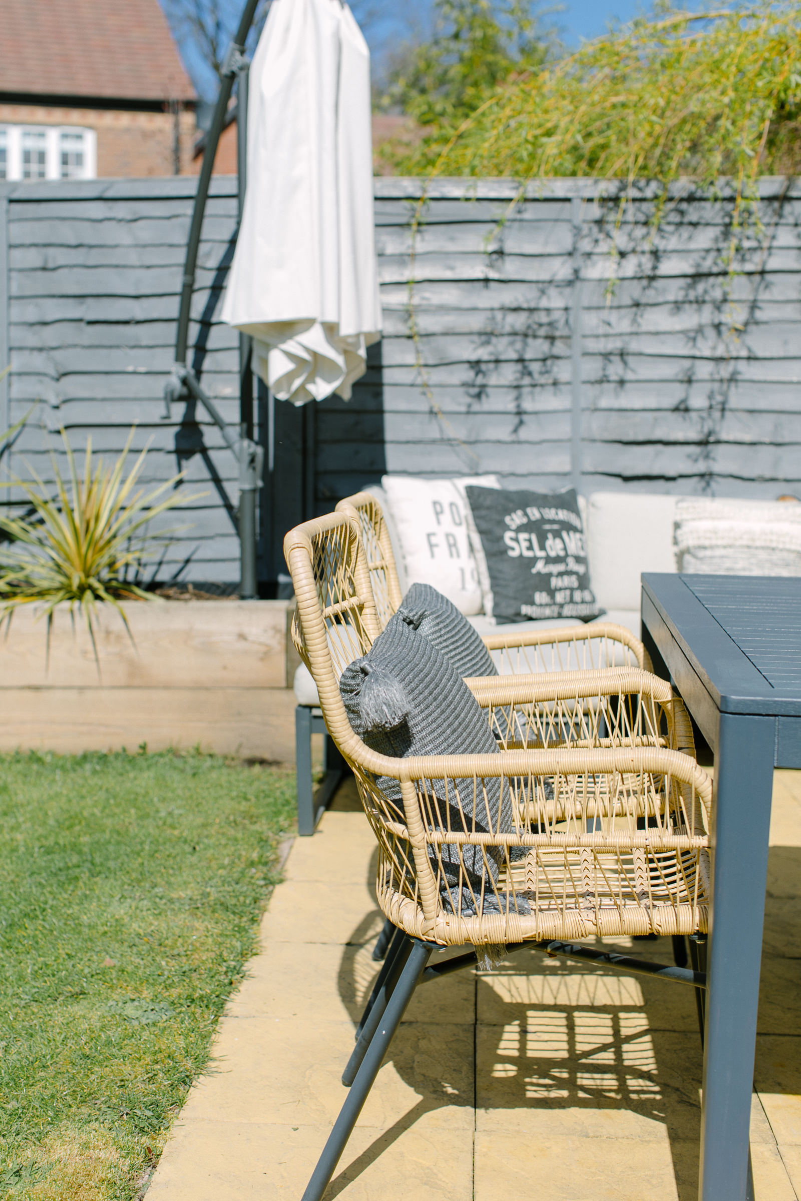 Rattan outdoor chairs and dark grey outdoor dining table in a small, modern garden