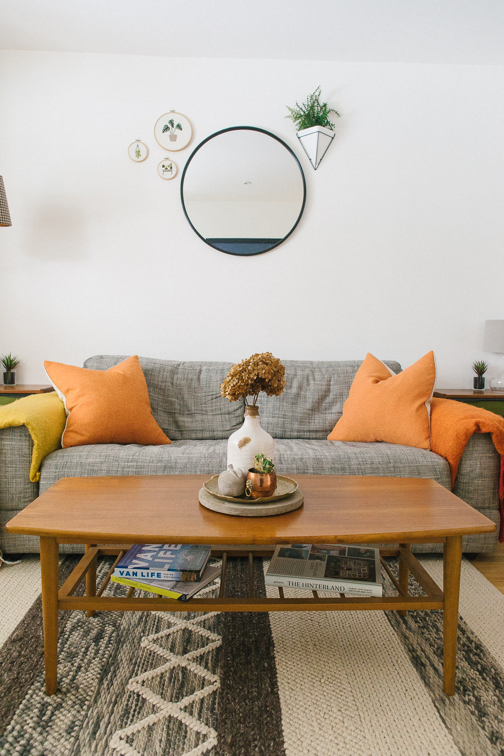 Grey fabric sofa from John Lewis with orange accent cushions and West Elm style circular mirror