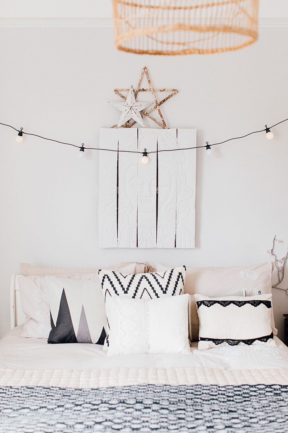 String lights above bed, monochrome cushions and vintage Buddha wall hanging